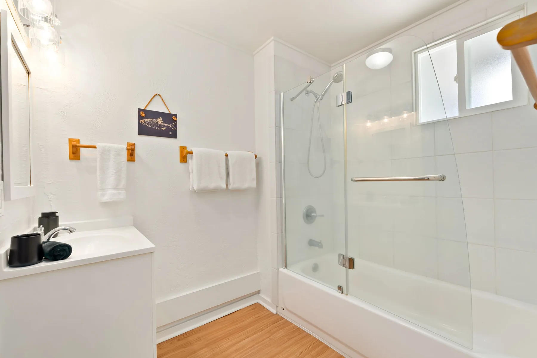 Un baño luminoso con una ducha de vidrio y un tocador blanco.