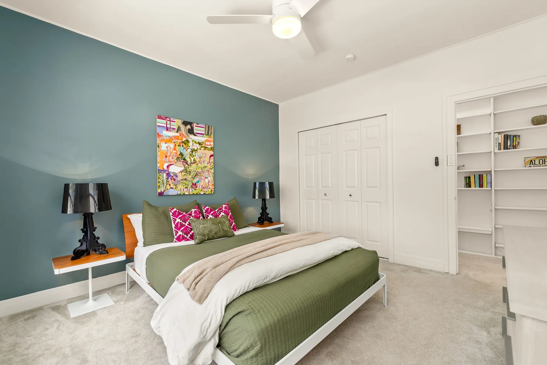 Un dormitorio con una cama, una pared verde azulado y estanterías empotradas.