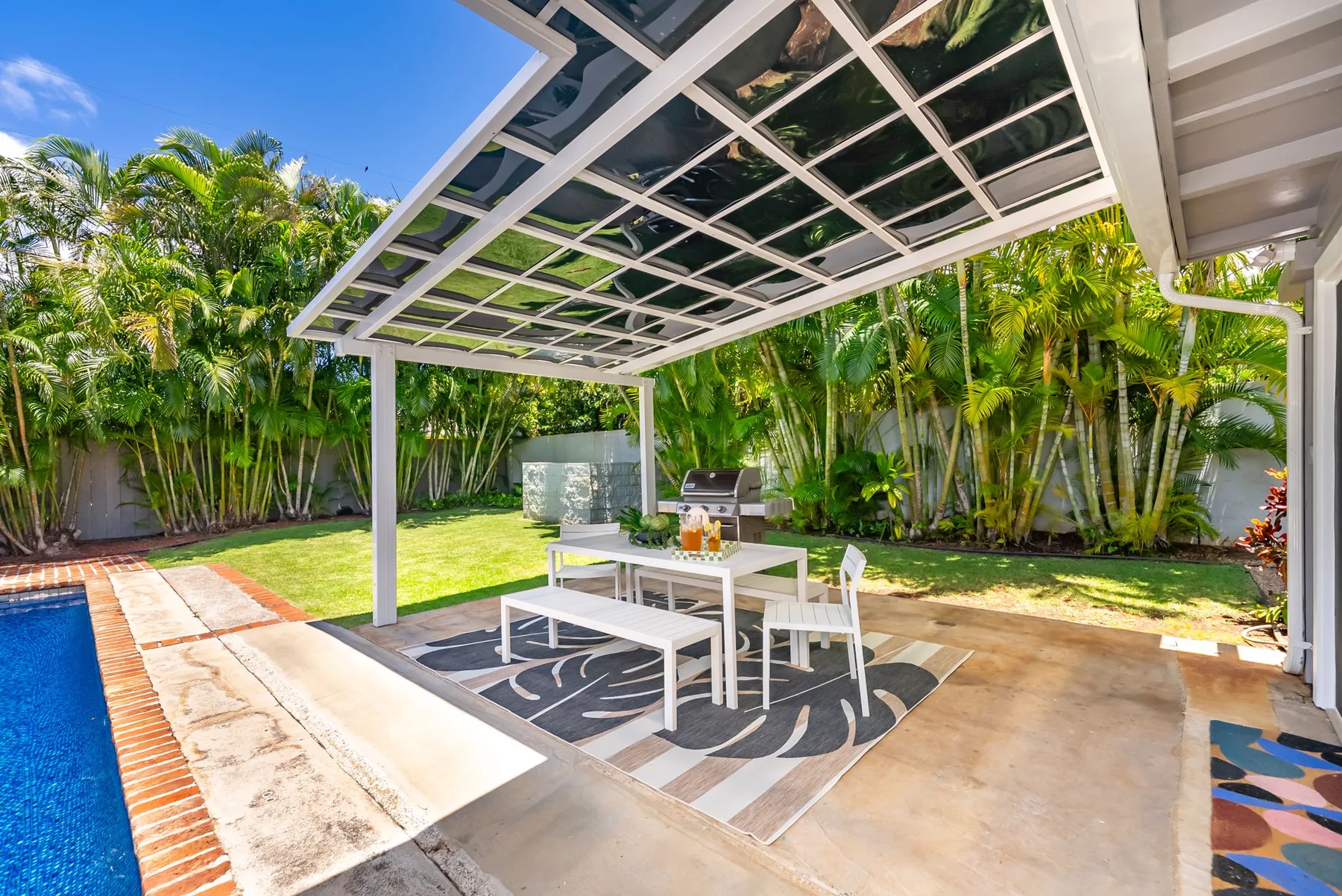 Un comedor al aire libre está bajo un patio cubierto junto a una piscina.