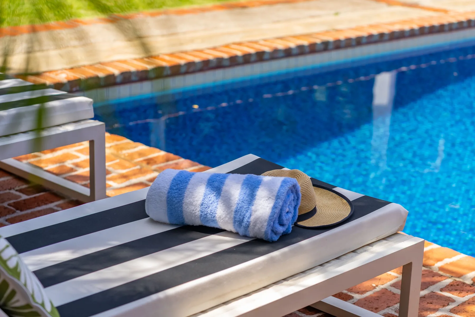 Una tumbona a rayas junto a una piscina tiene una toalla doblada azul y blanca.