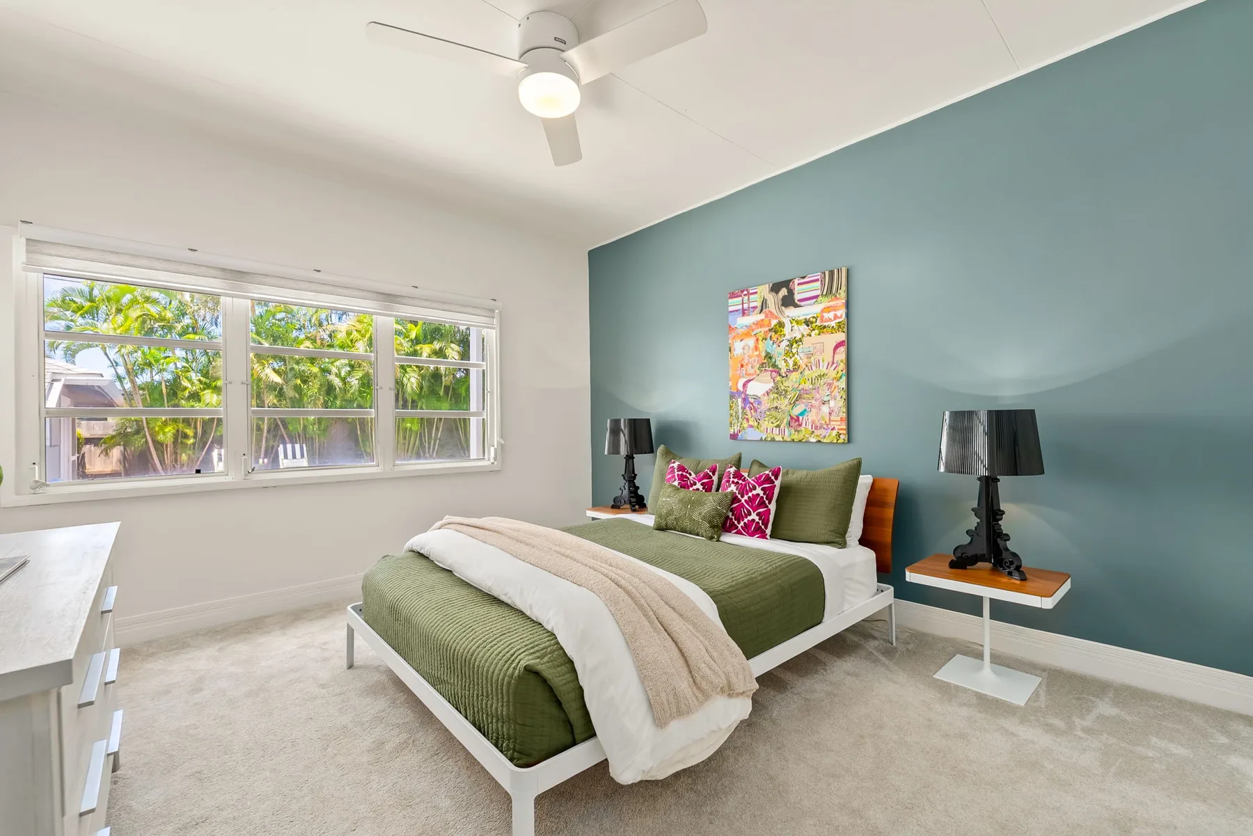 Un dormitorio con una cama junto a una pared verde azulado y una ventana grande.