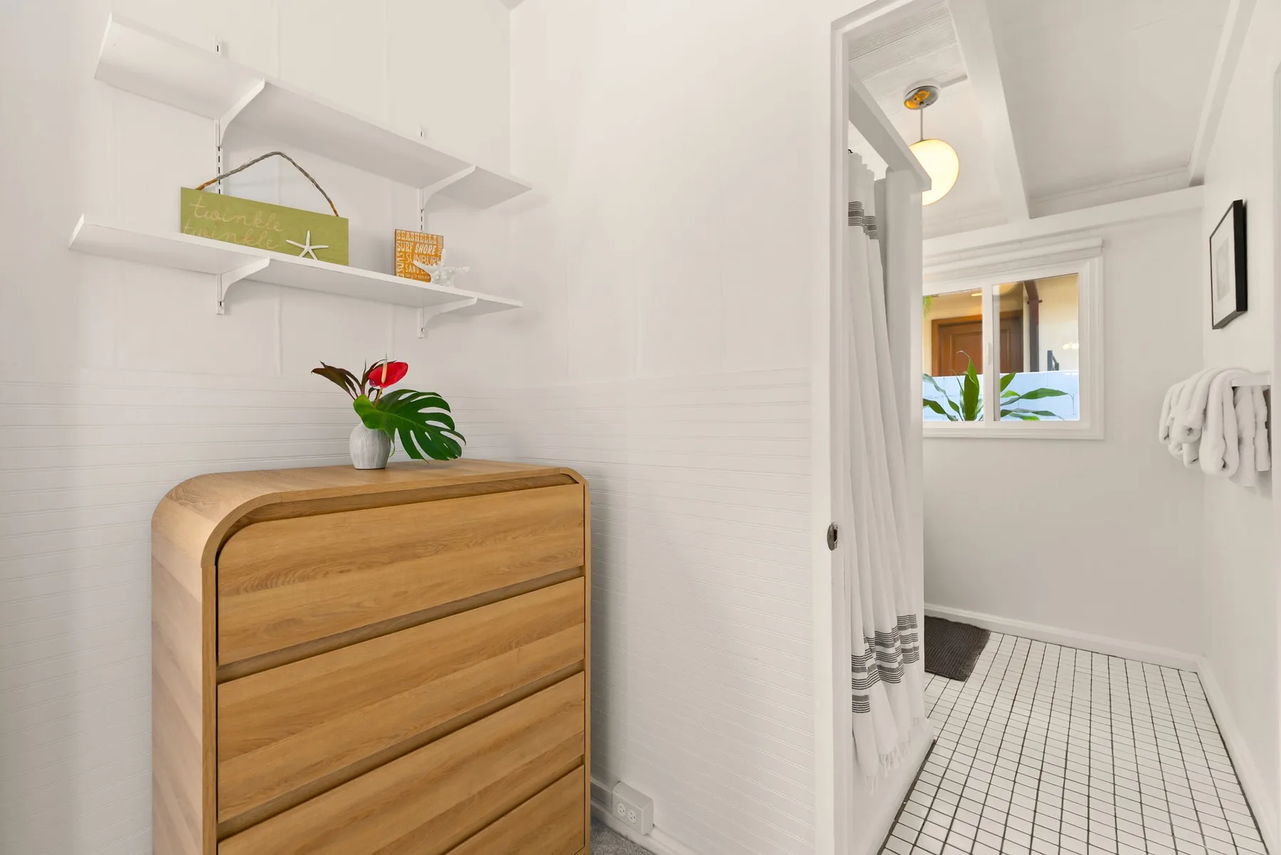 Un baño luminoso tiene una cómoda de madera junto a una ducha y una ventana pequeña.