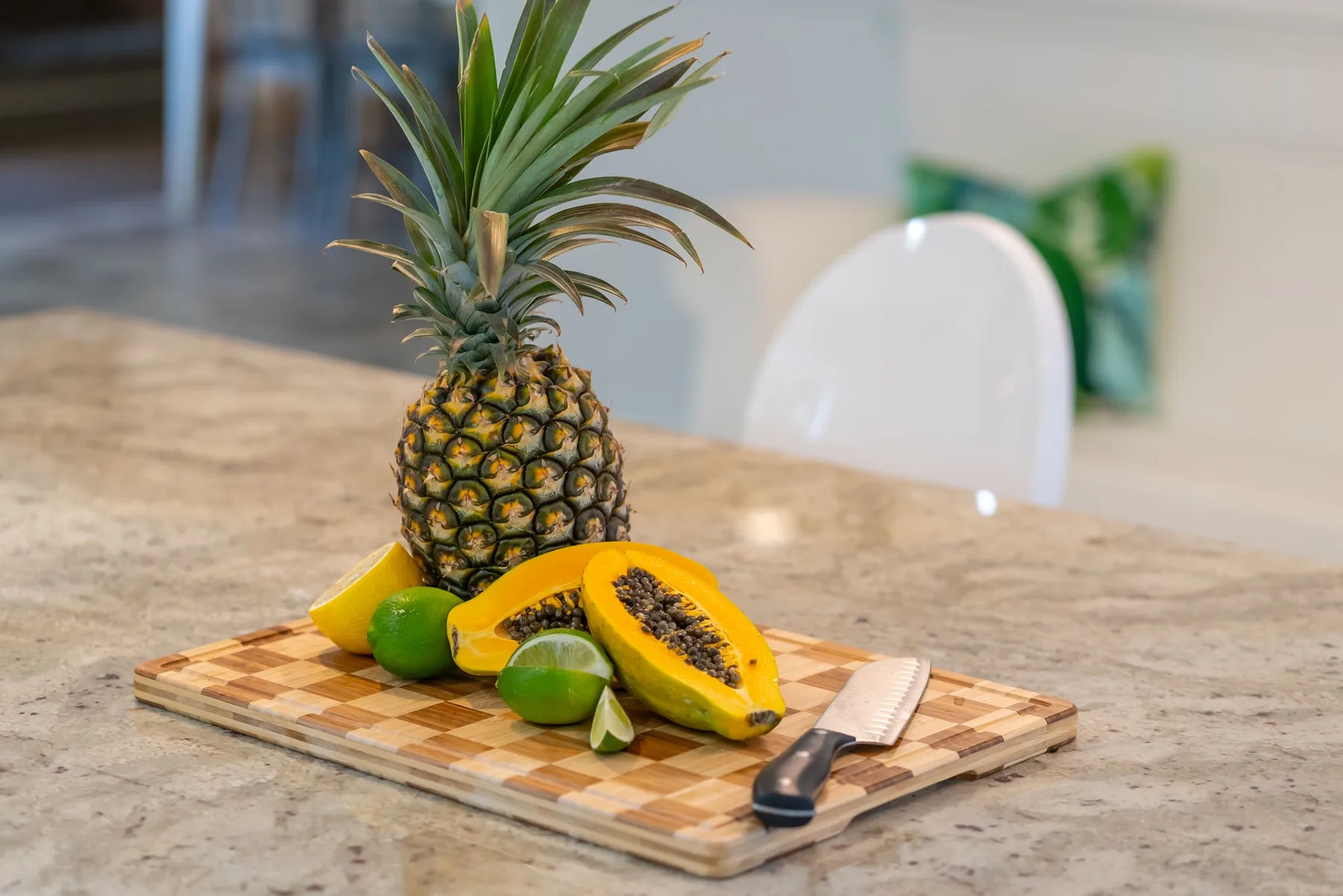Una encimera de cocina muestra una piña, una papaya y una lima sobre una tabla de cortar.