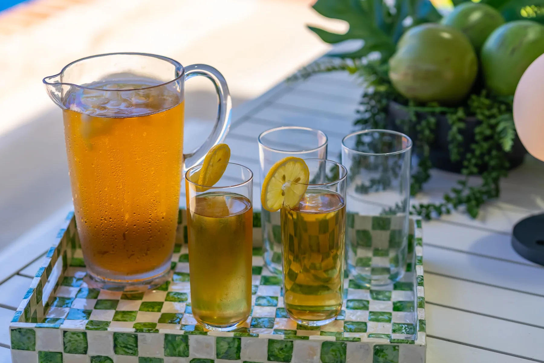 Una jarra y vasos de té helado están sobre una bandeja junto a frutas verdes.
