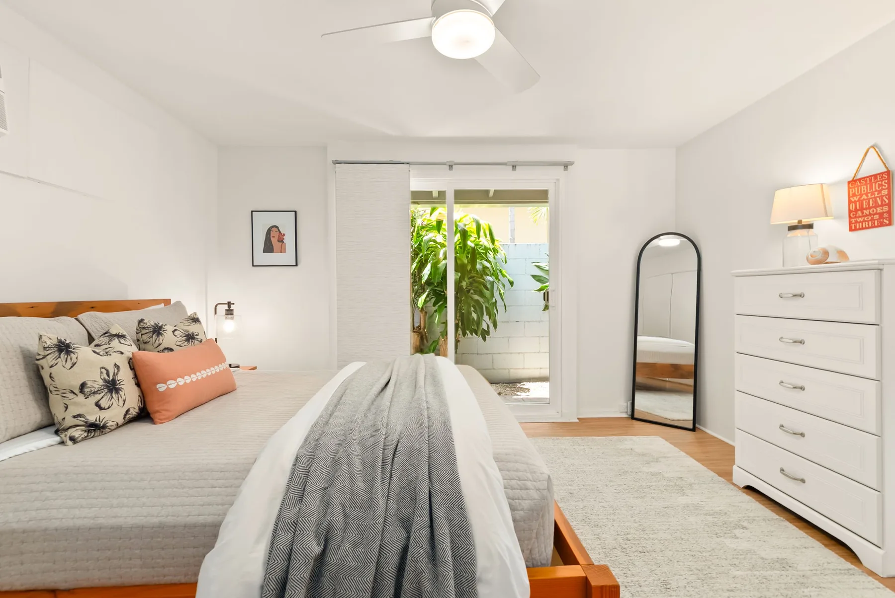 Un dormitorio luminoso con una cama, una cómoda y puertas de vidrio que dan a un balcón.