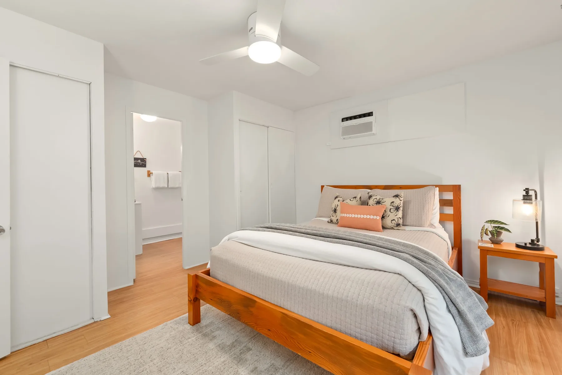 Un dormitorio luminoso con una cama, una mesita de madera y un ventilador de techo.