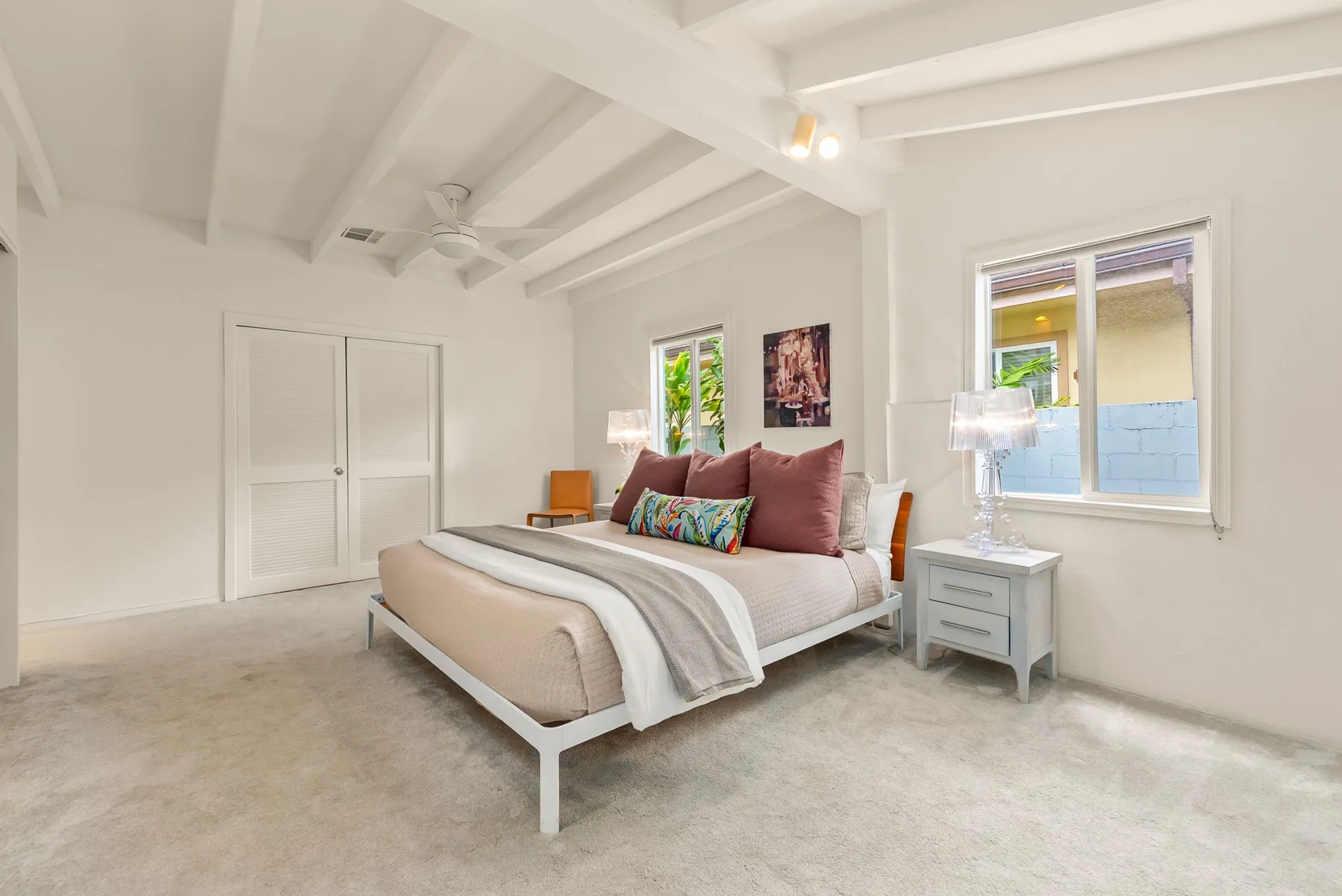 Un dormitorio luminoso con una cama, mesitas de noche y ventanas.