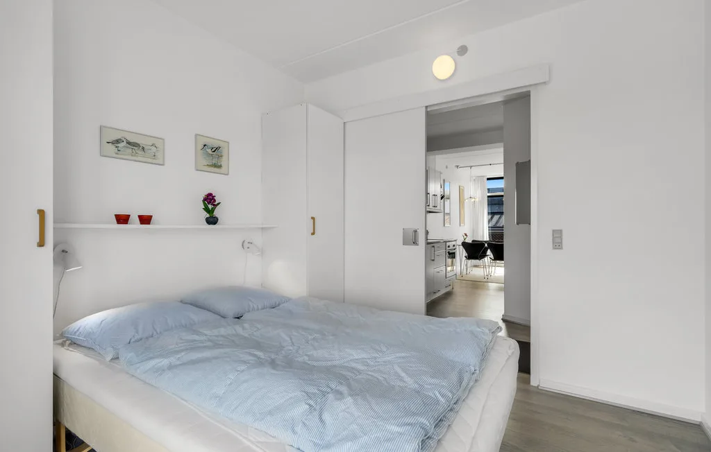 Un dormitorio con una cama y ropa de cama azul claro, con una puerta abierta a otra habitación.