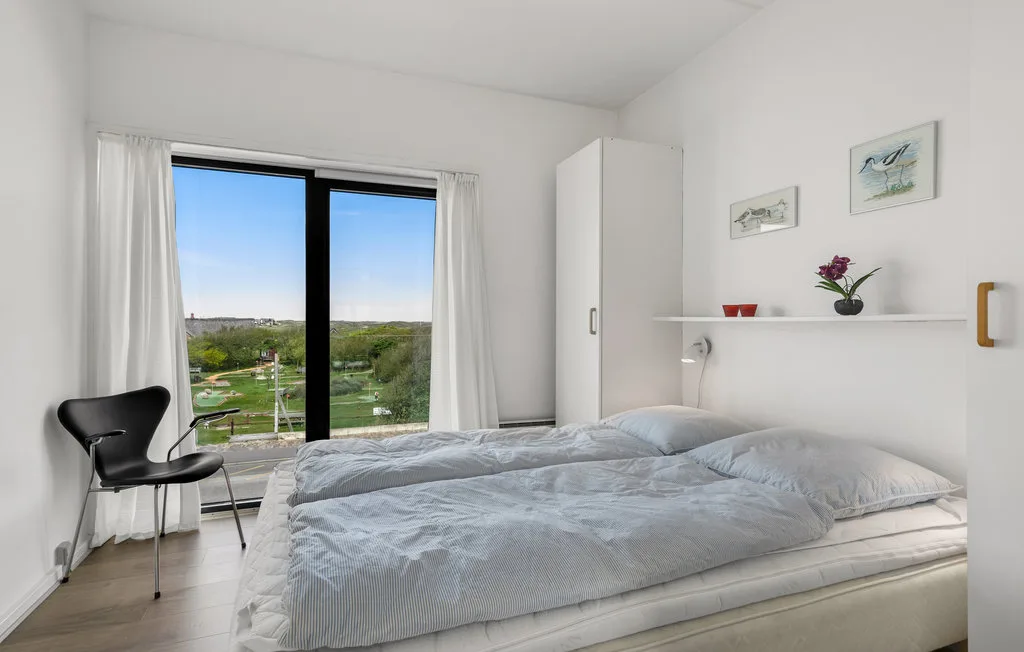 Un dormitorio luminoso con una cama junto a una gran ventana que da a una zona verde.