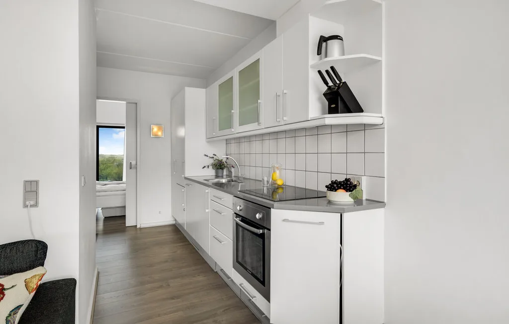 Una cocina luminosa con gabinetes blancos, salpicadero de azulejos y horno integrado.
