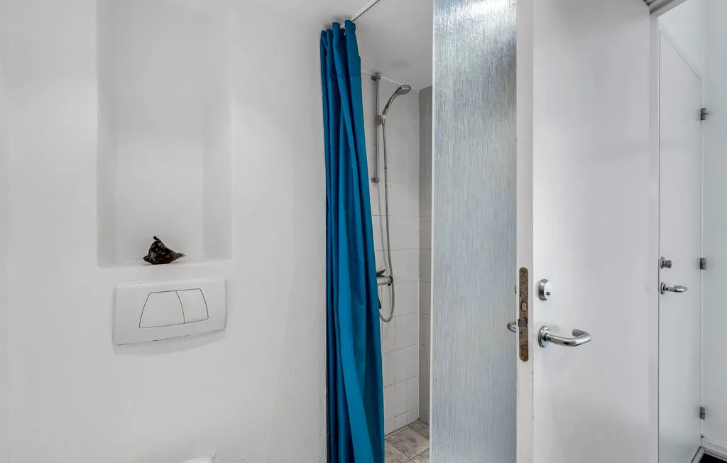 Una ducha de baño queda parcialmente cubierta por una cortina azul junto a una puerta blanca.