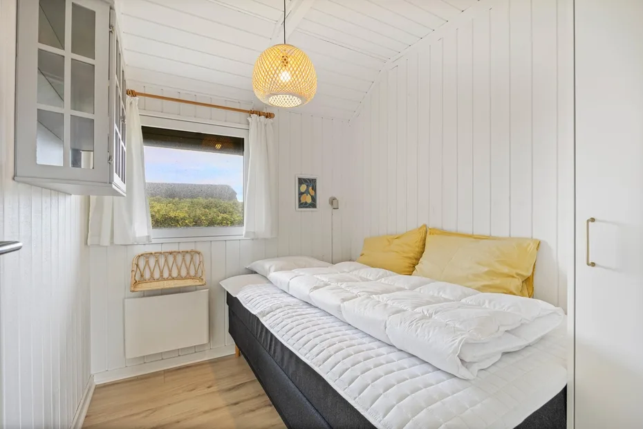 A bright bedroom with a bed dressed in white bedding and yellow pillows.