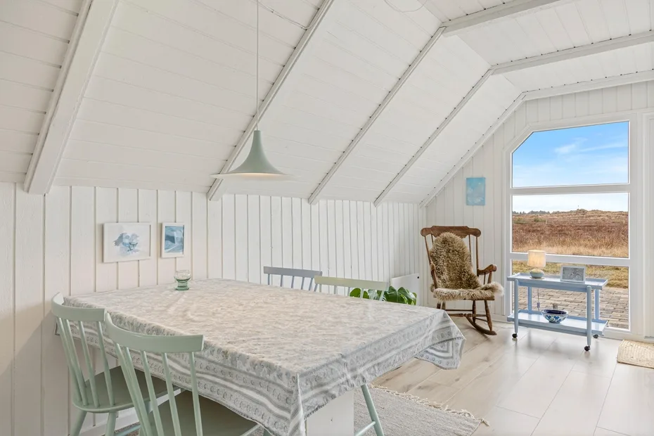 A bright dining area with a long table and a large window overlooking open land.