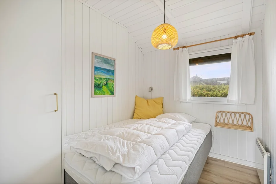 A bright bedroom with a bed beneath a window overlooking green hills.