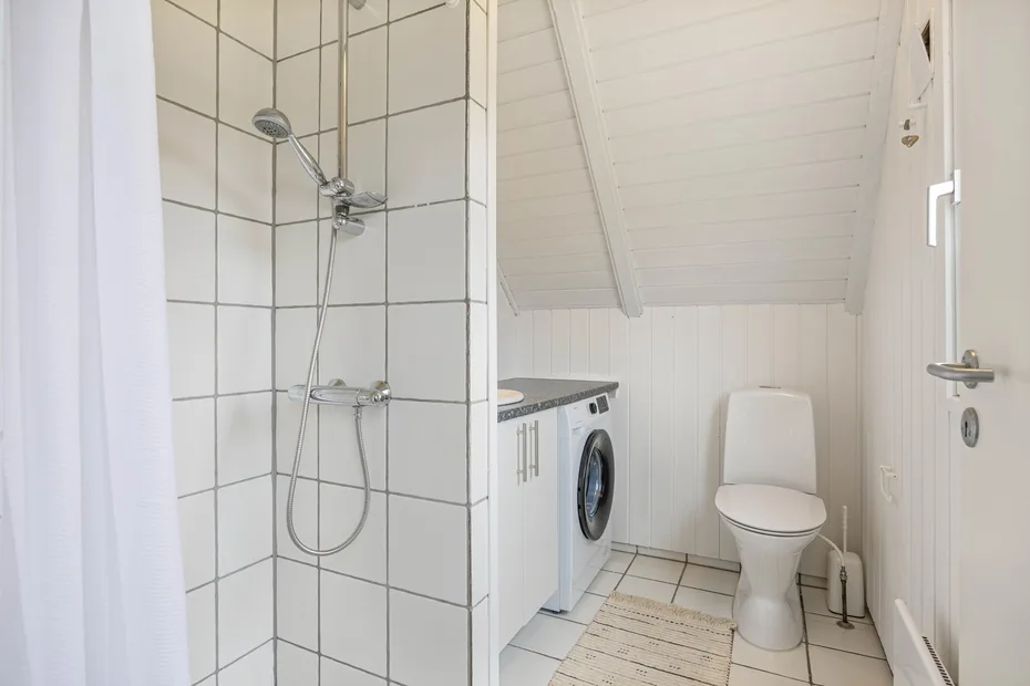 A compact bathroom with a shower, toilet, and washing machine.