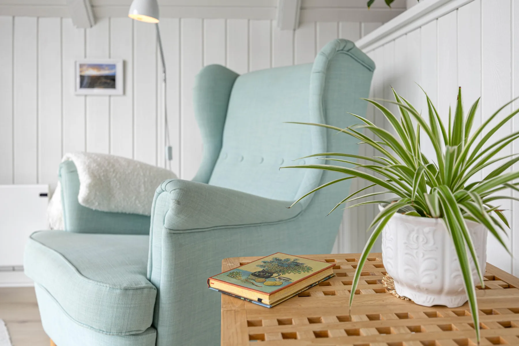 A living room with a pale blue armchair beside a wooden table and potted plant.