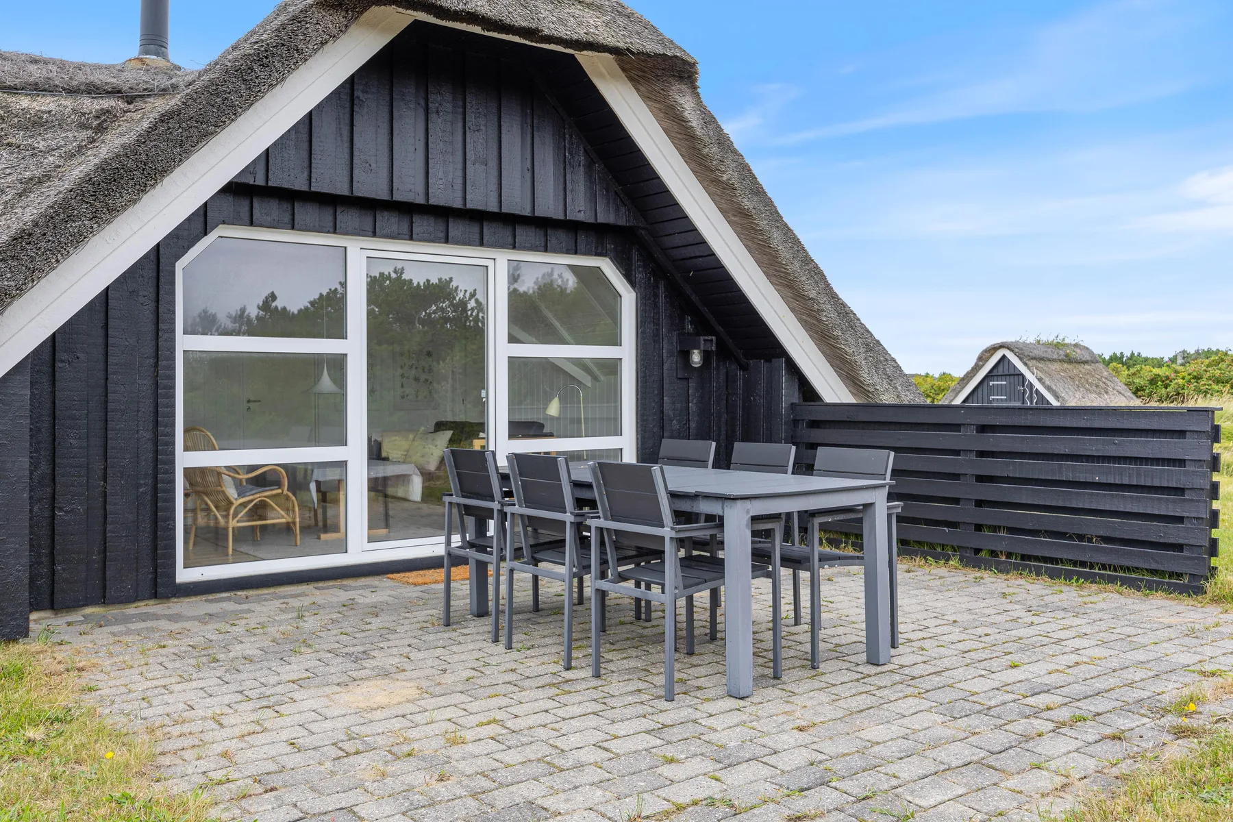 A paved patio with outdoor dining furniture beside a dark timber house.