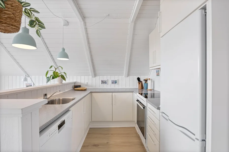 A bright white kitchen with counters, cabinets, and a stainless steel sink.