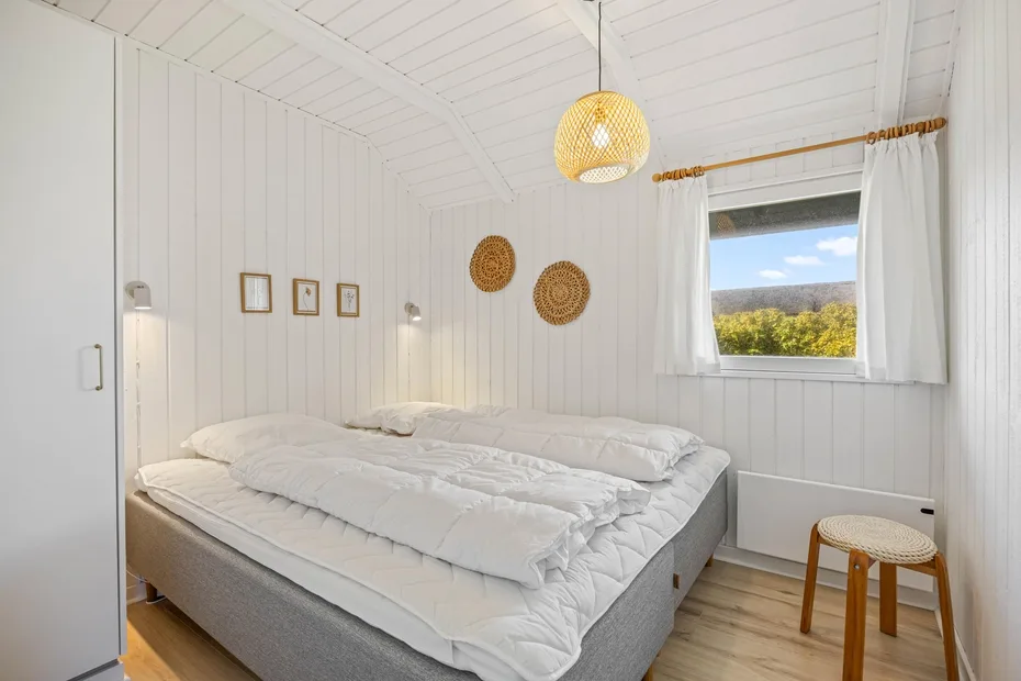 A bright bedroom with a neatly made bed and a window overlooking greenery.