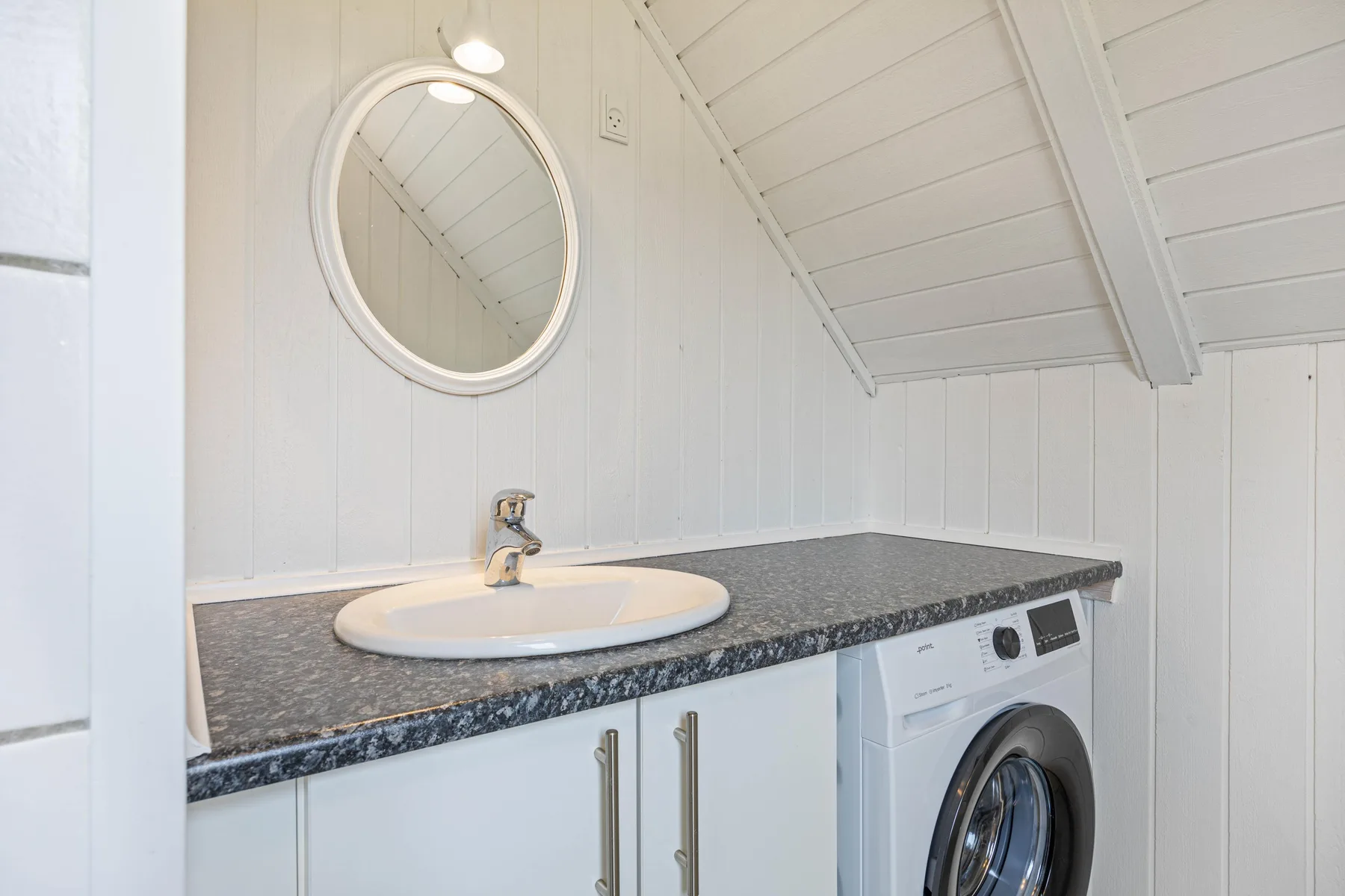 A bright bathroom vanity with a round mirror and washing machine beneath the counter.
