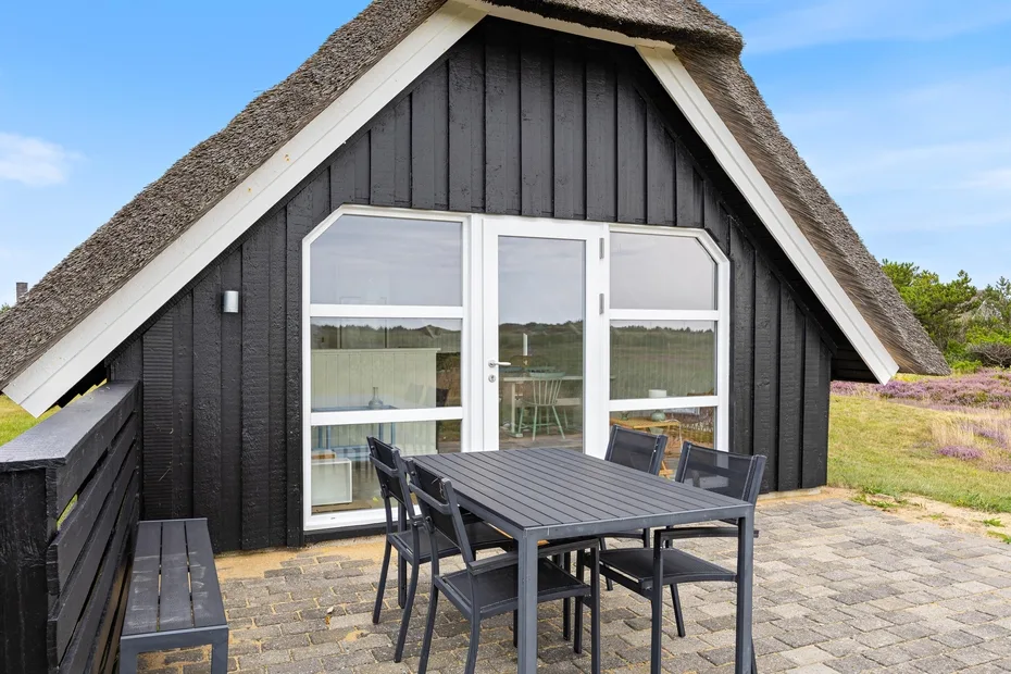 An outdoor patio beside a dark cottage, with a dining table and chairs.