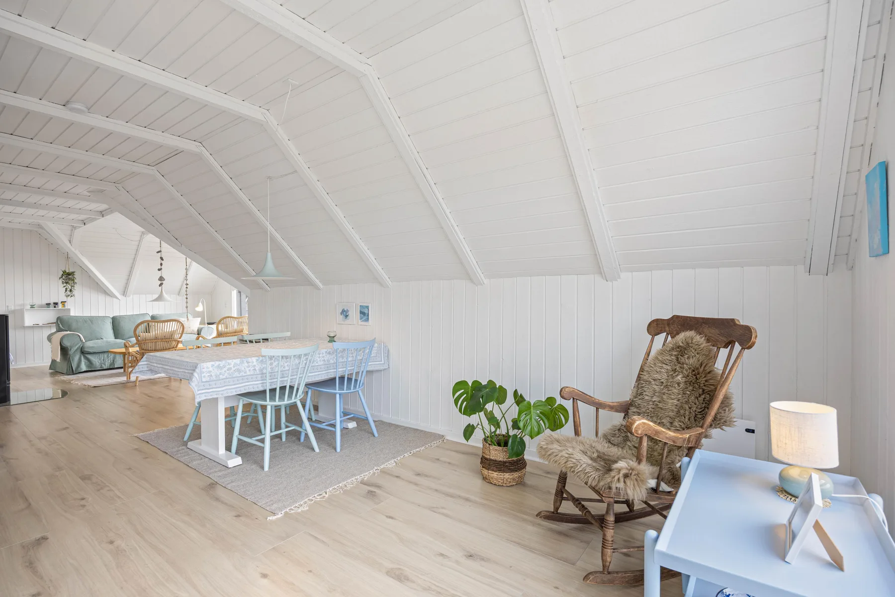 A bright dining area with a table and seating beneath a sloped white ceiling.