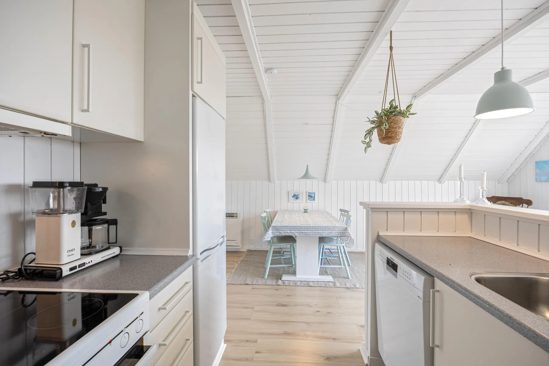 A bright kitchen opens onto a dining area with a table and chairs.