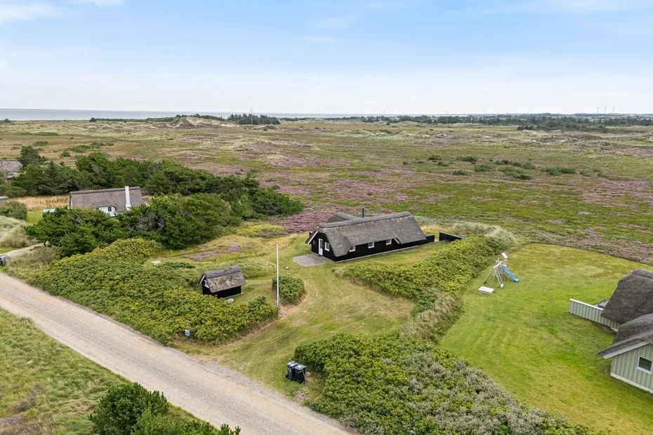 Aerial view of a dark-roofed house beside a grassy yard and open fields.