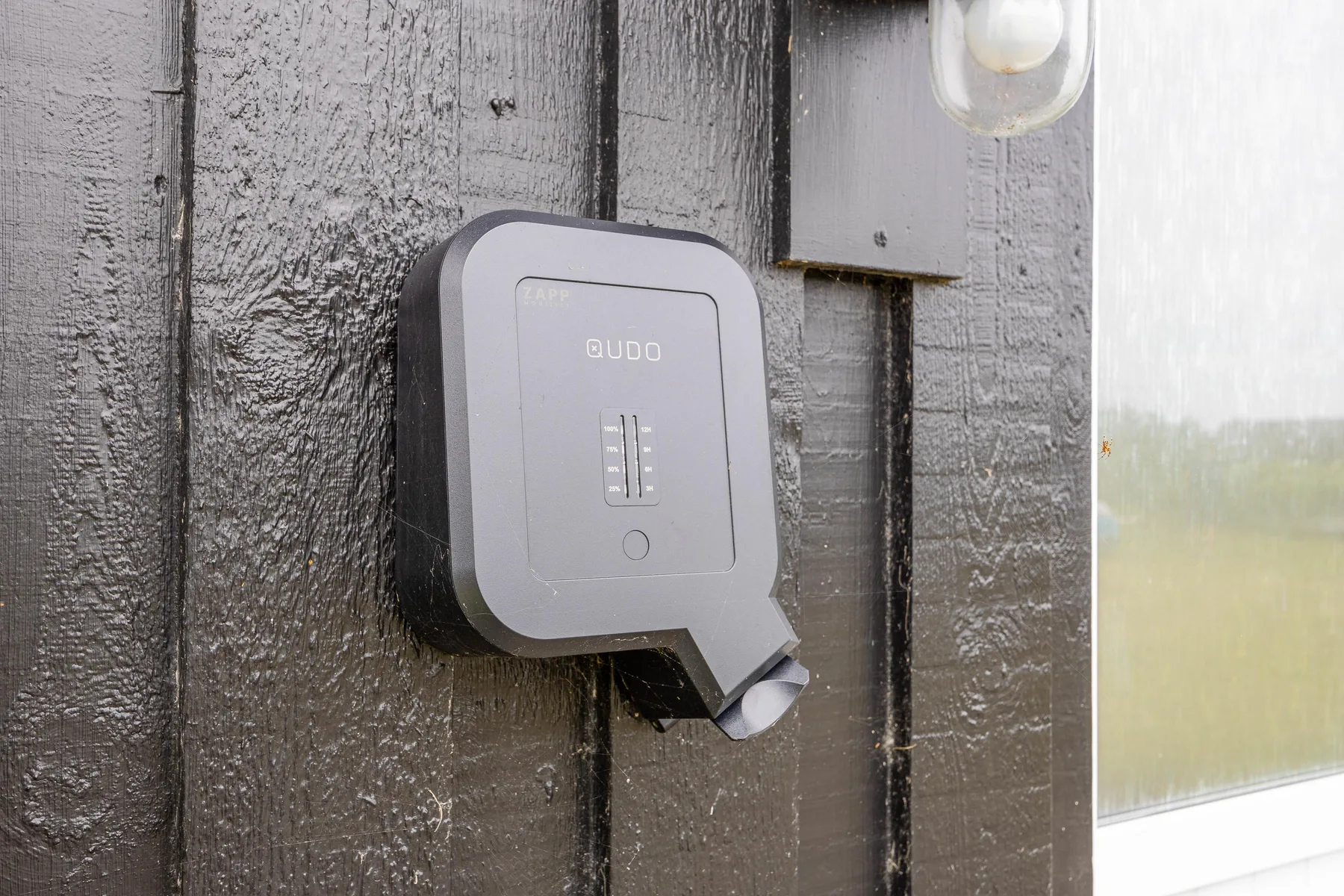 A keypad is mounted on a dark wooden exterior wall beside a window.
