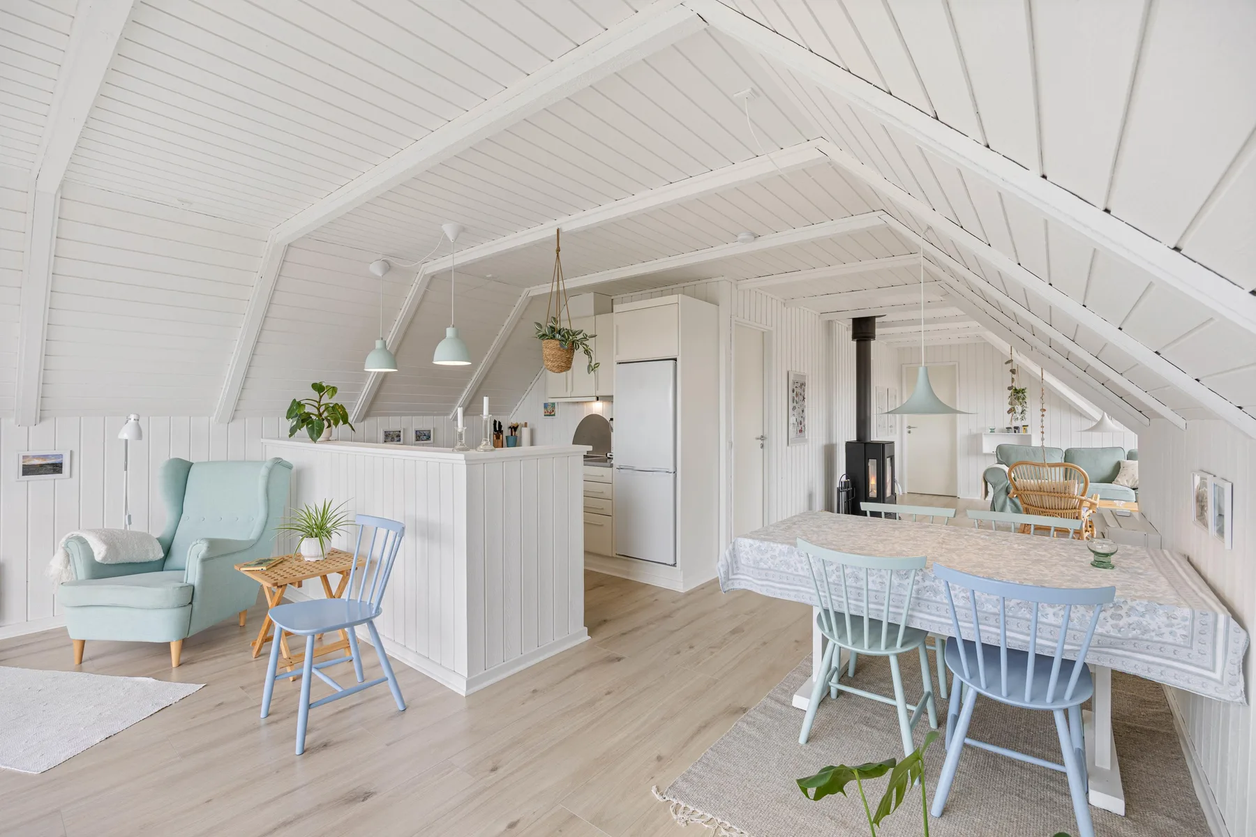A bright attic dining and kitchen area with a table, chairs, and sloped white ceiling.