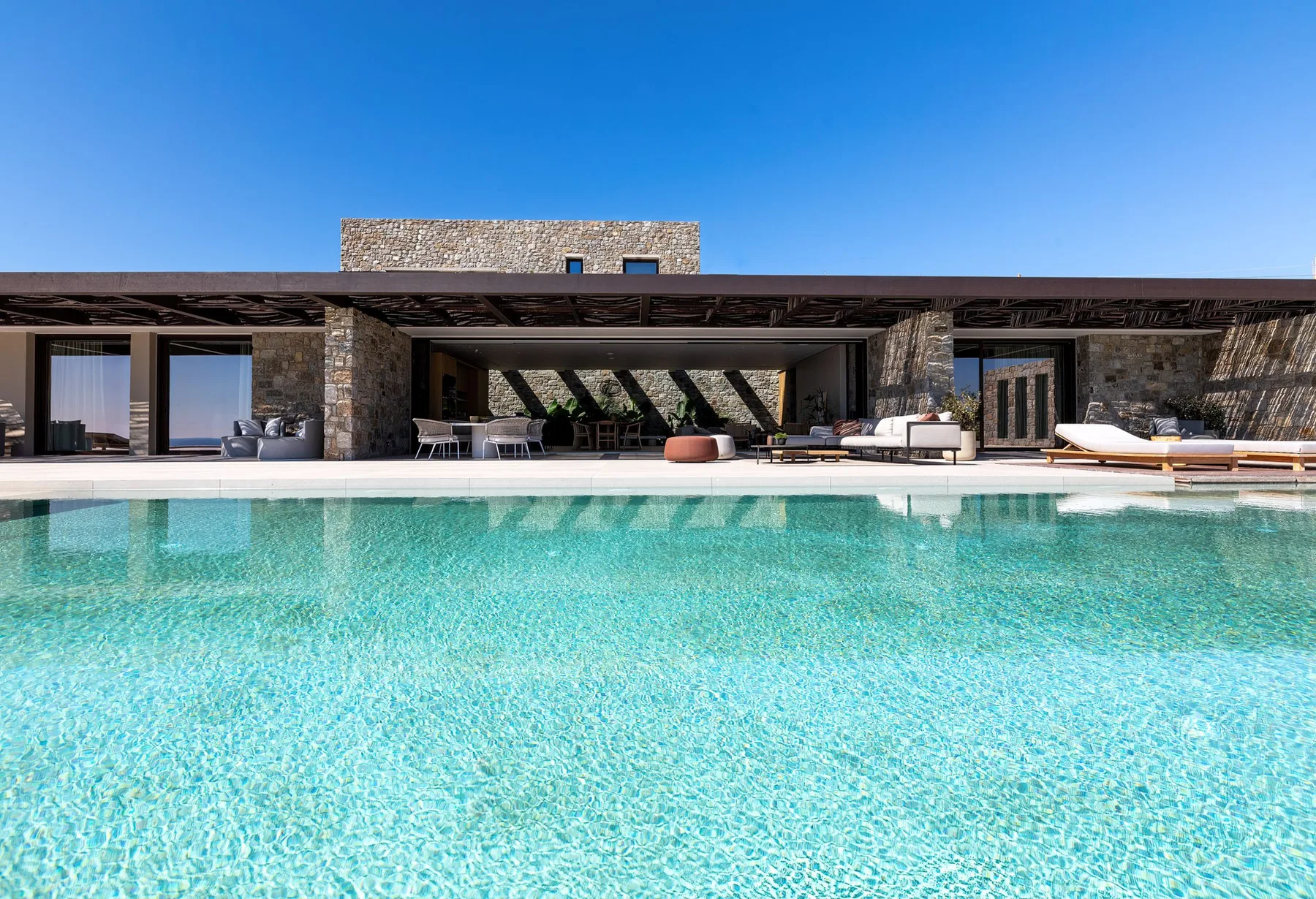 Una casa moderna da a una piscina, con asientos al aire libre junto al borde.