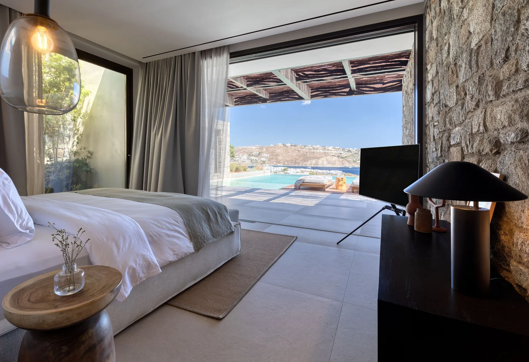 A bedroom opens onto a patio with a pool and distant hills.