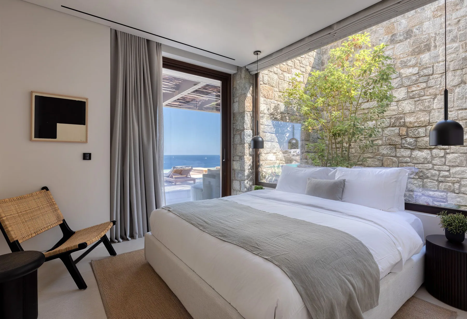 A bright bedroom with a large bed beside a window overlooking the sea.