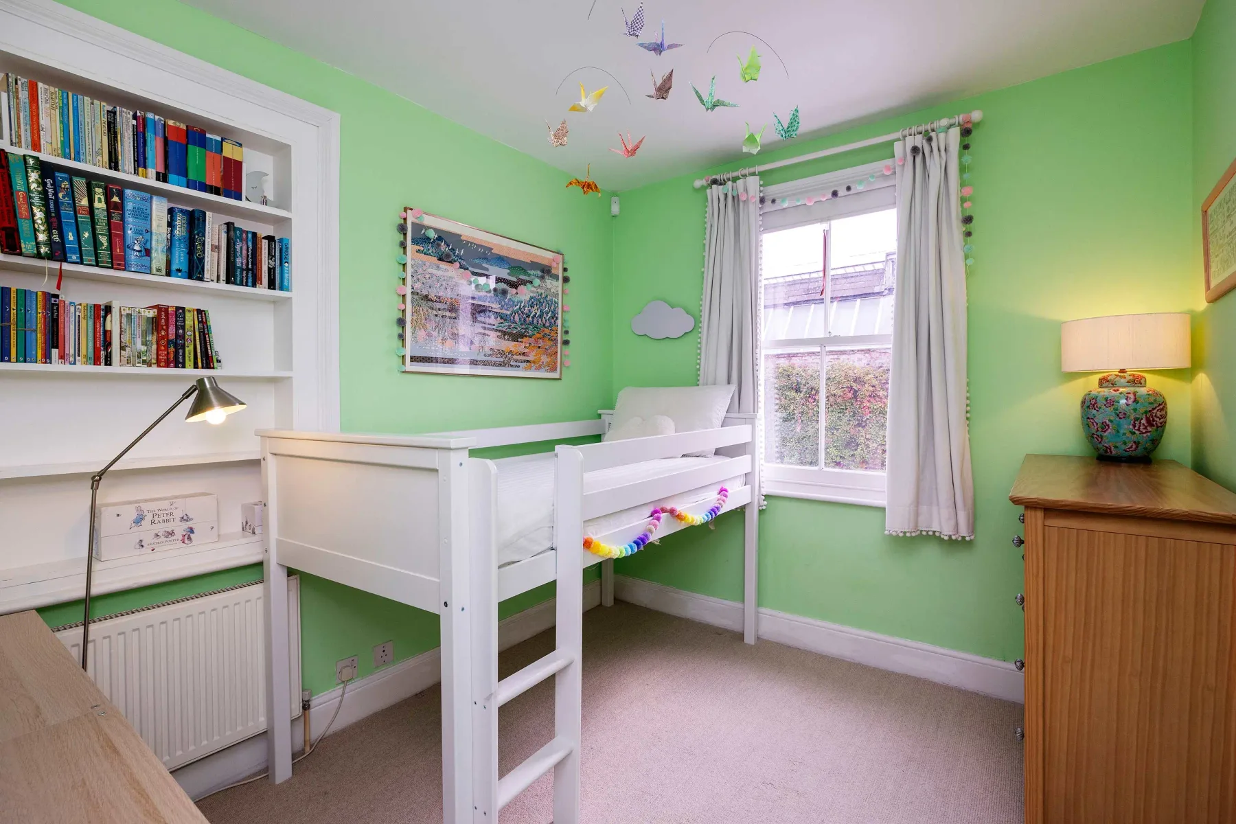 A green bedroom with a white bed, bookshelves, and a window.