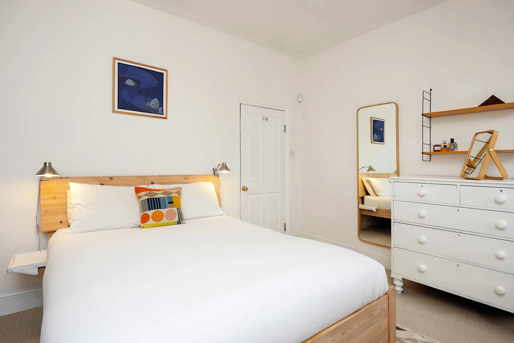 A bright bedroom with a white bed, wooden headboard, and framed wall art.