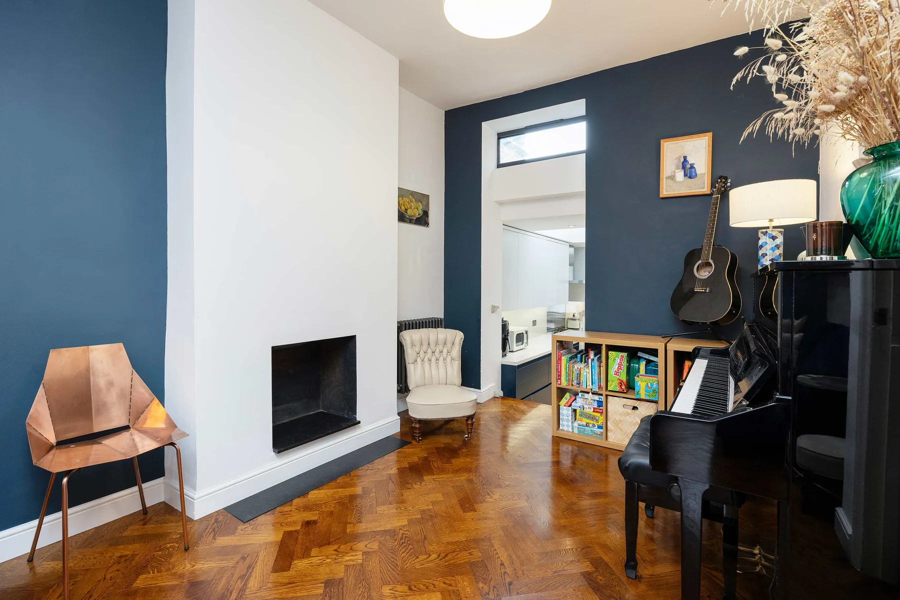 A music room with a piano, guitar, and colorful bookcase.