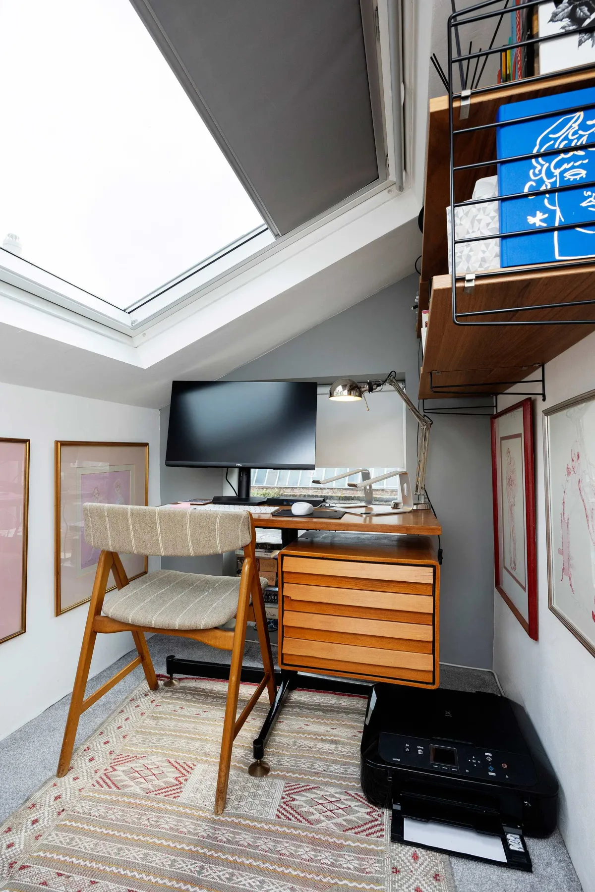 A compact desk area beneath a large skylight, with a chair and wall-mounted screen.