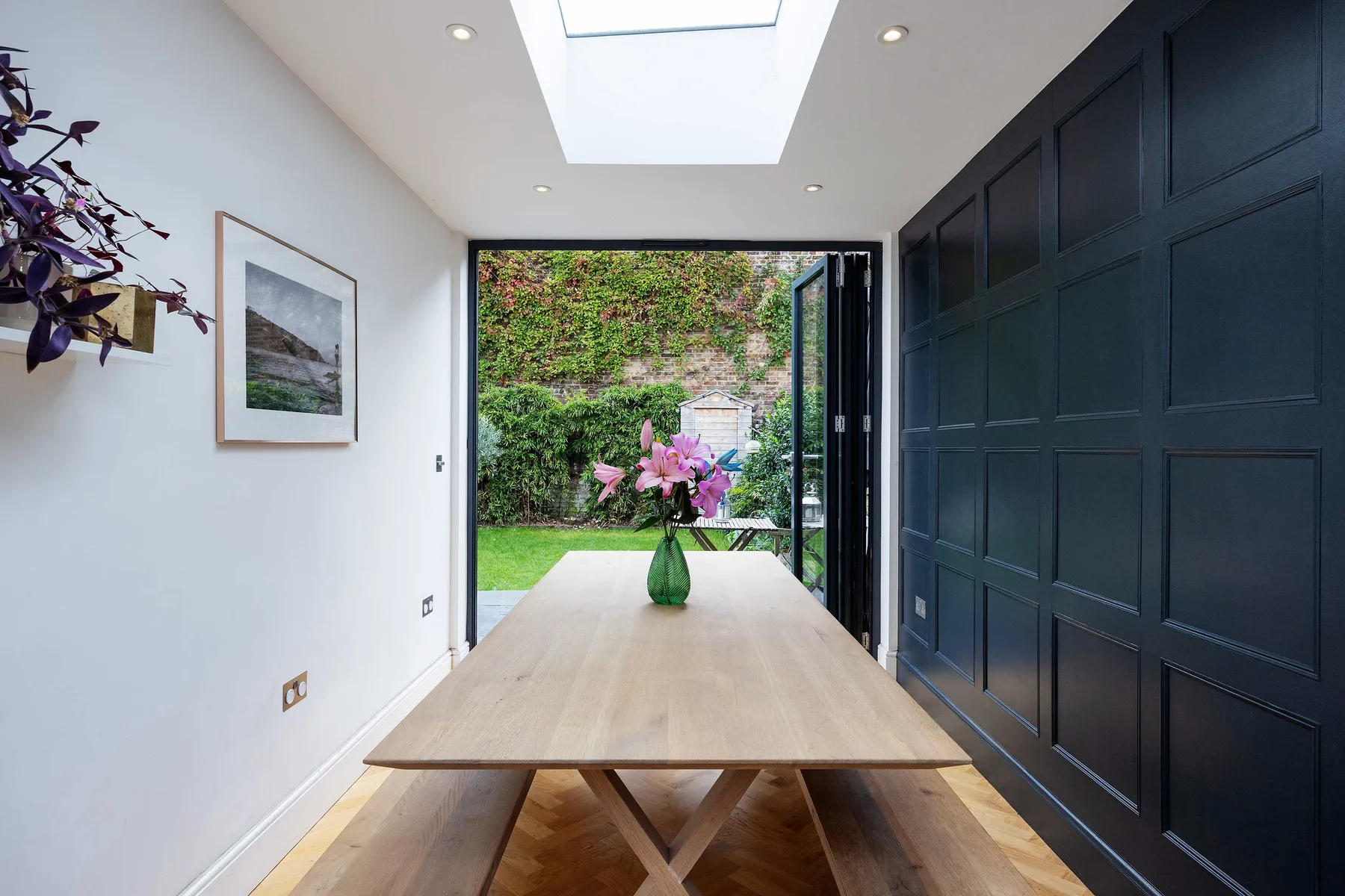 A bright entryway with a long wooden table and an open doorway to the garden.