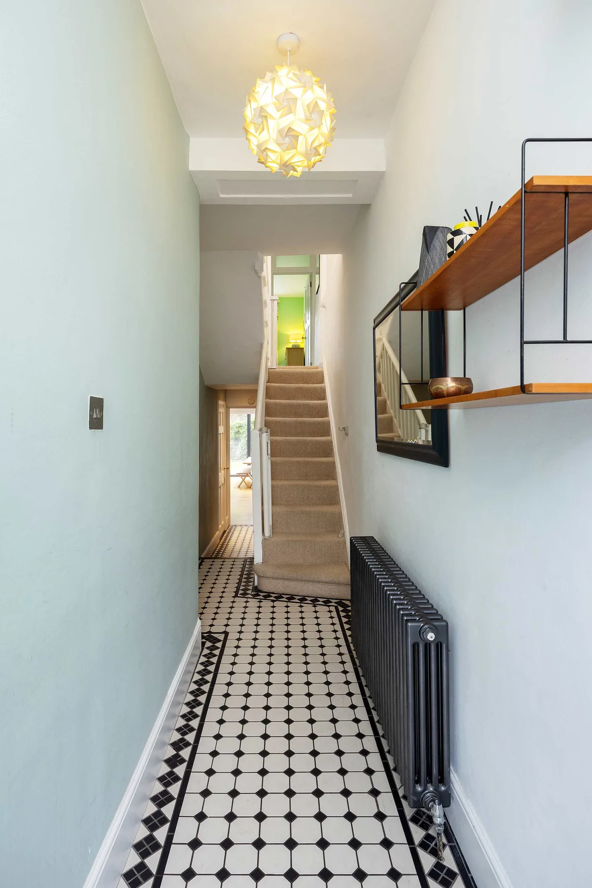 A narrow hallway with a patterned tile floor, radiator, and staircase.