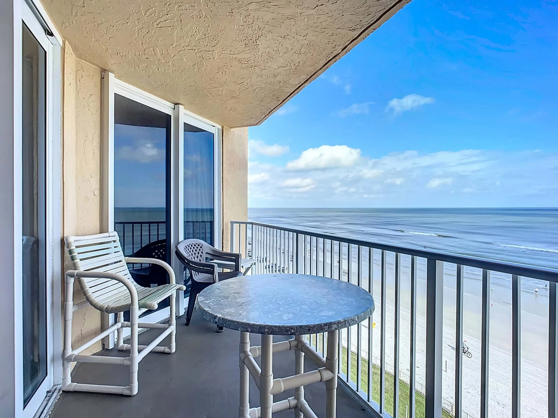 A balcony with outdoor seating and a table overlooks the beach and ocean.