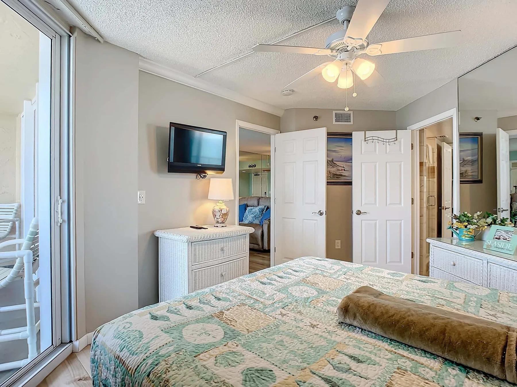A bedroom with a patterned bedspread, dresser, and ceiling fan.