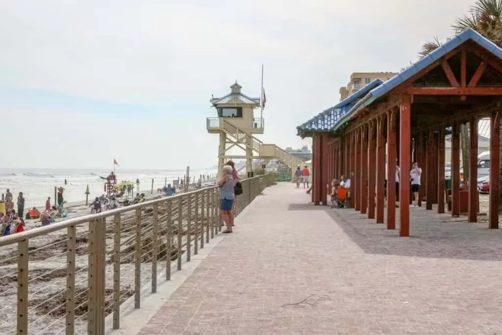 A seaside promenade runs beside a wooden pavilion and beach.