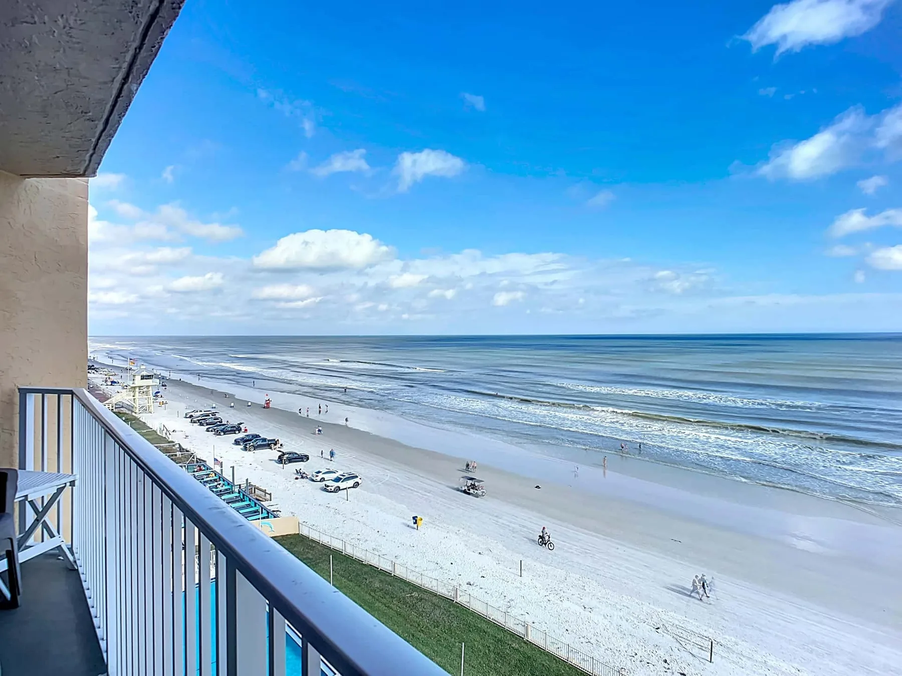 A balcony overlooks a sandy beach and ocean under a bright blue sky.