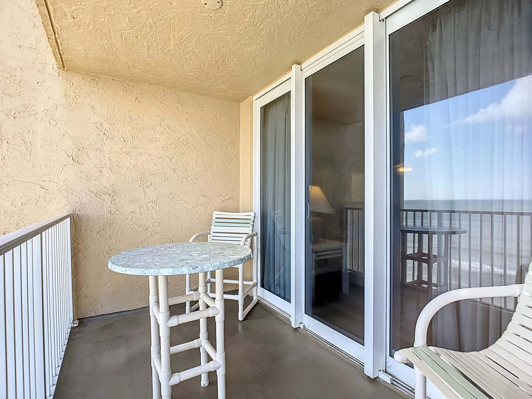 A small balcony with a round table and seating beside sliding glass doors.
