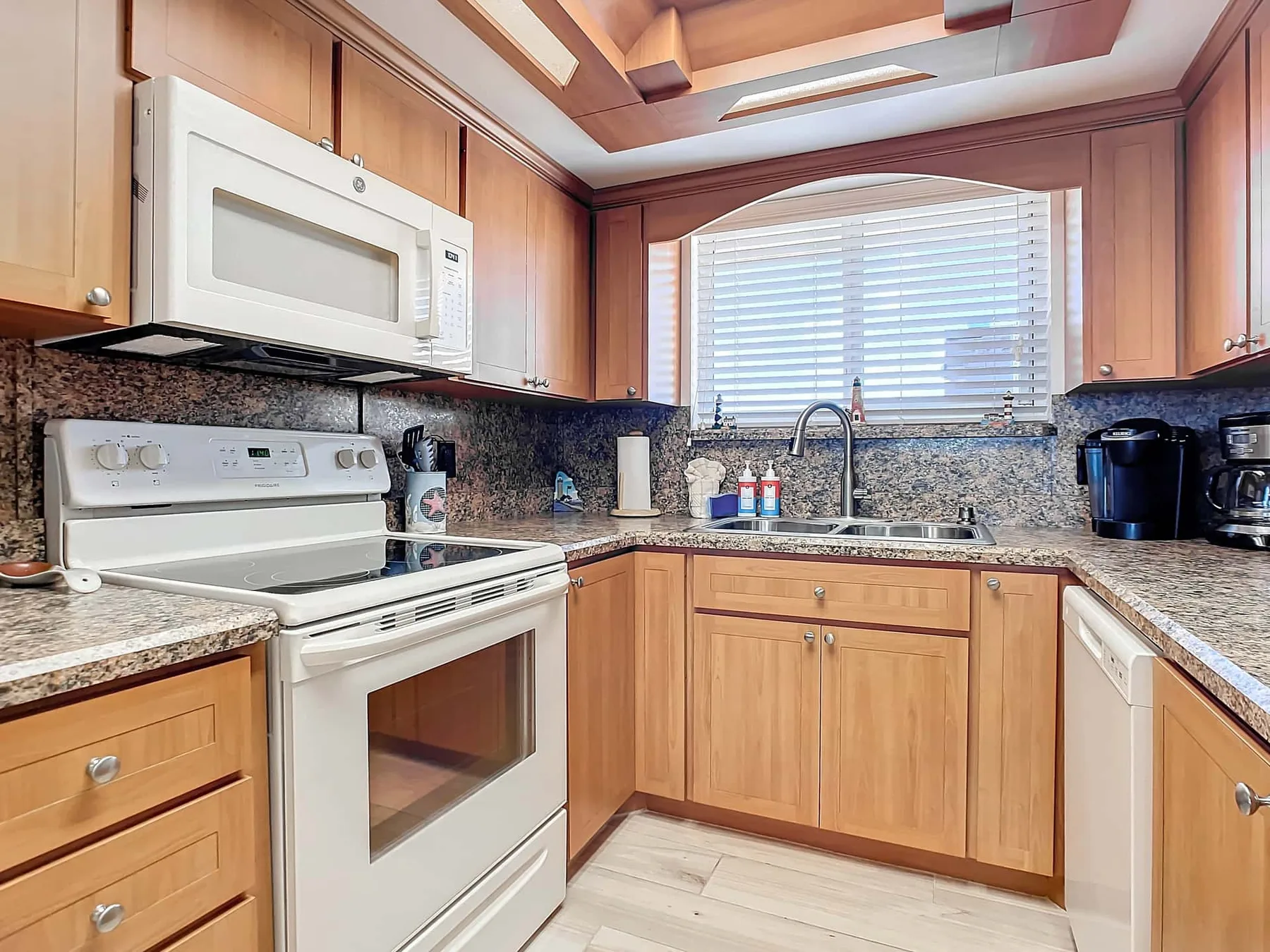 A bright kitchen with wooden cabinetry, a stove, and a sink beneath a window.