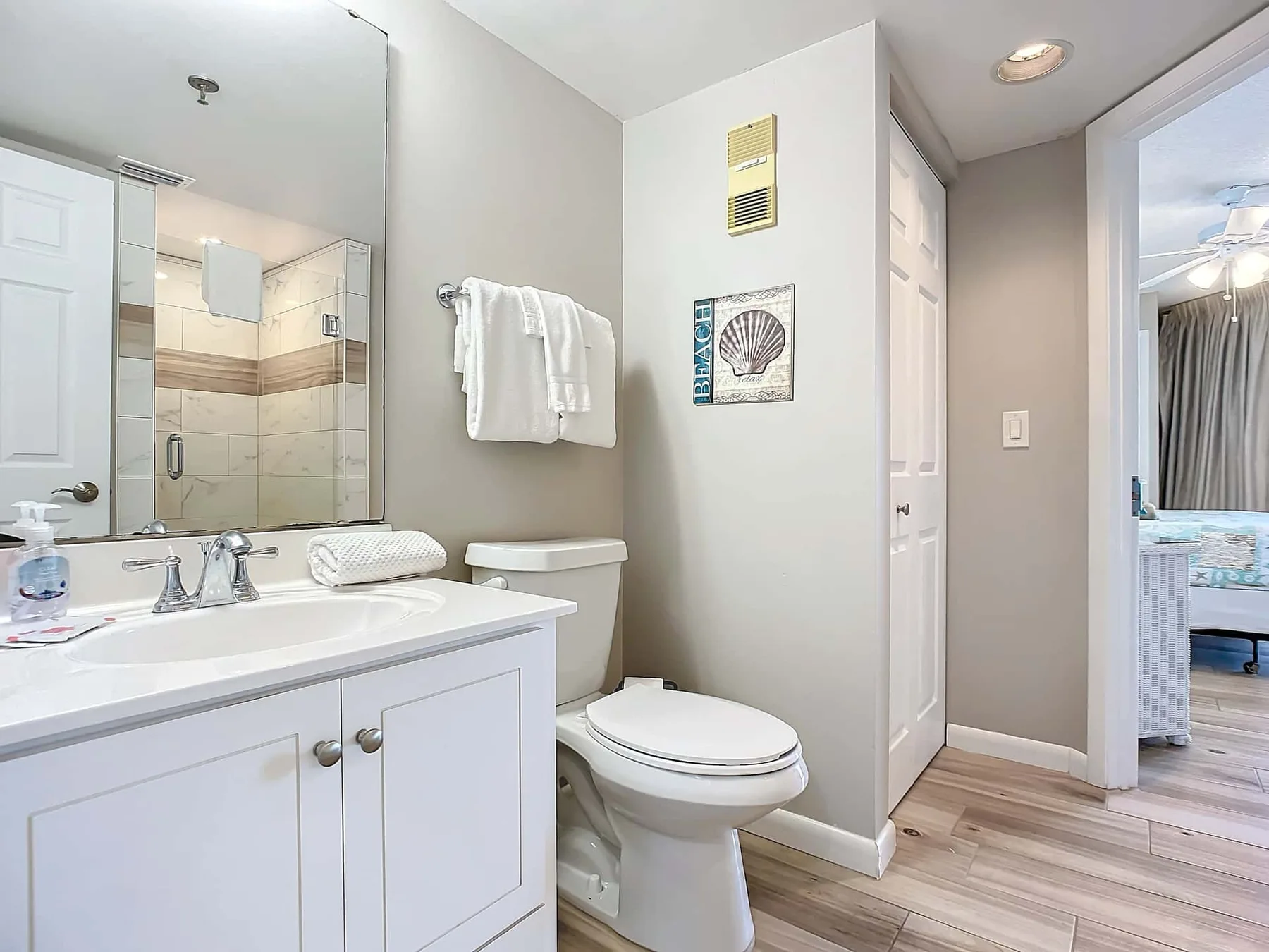 A bright bathroom with a sink, toilet, and doorway to a bedroom.