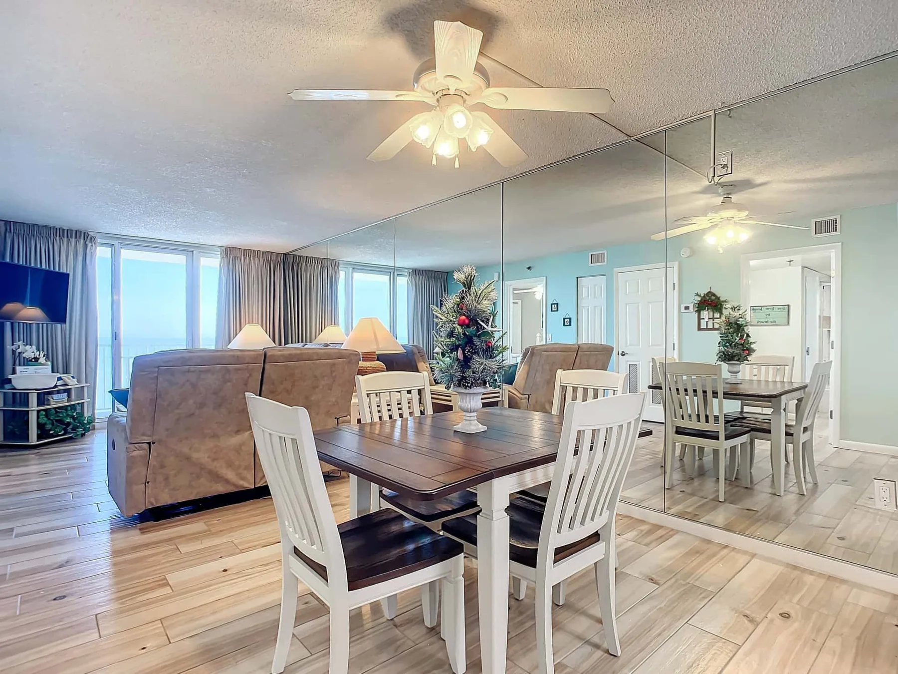 A dining area with a wooden table and white chairs beside a mirrored wall.