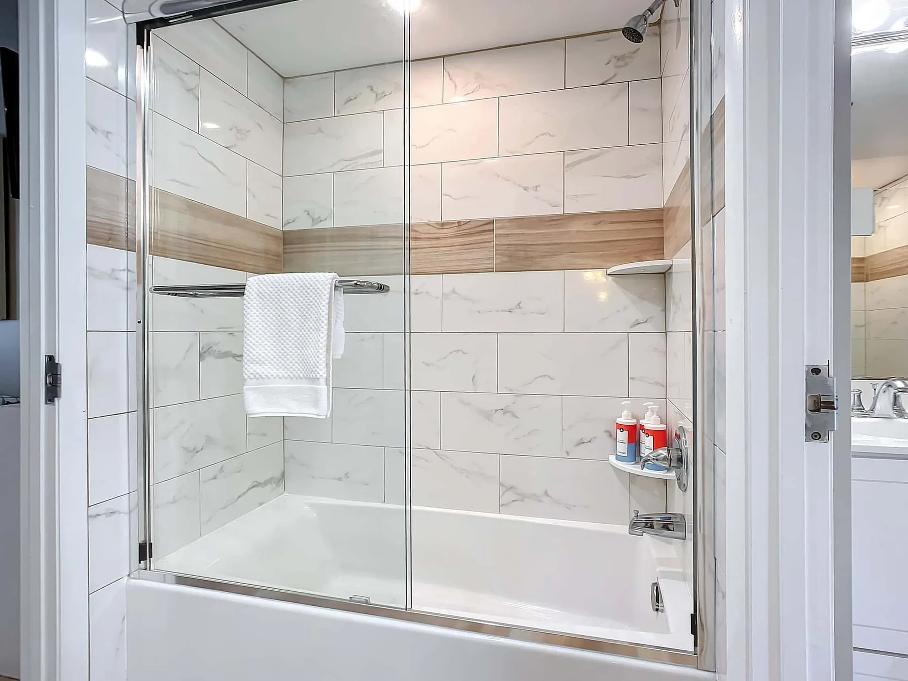 A tiled bathroom shower with a glass screen and a towel hanging nearby.