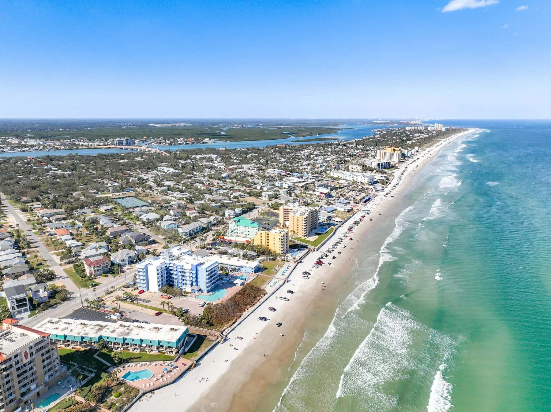 An aerial view shows a coastal beach, ocean, and nearby buildings.
