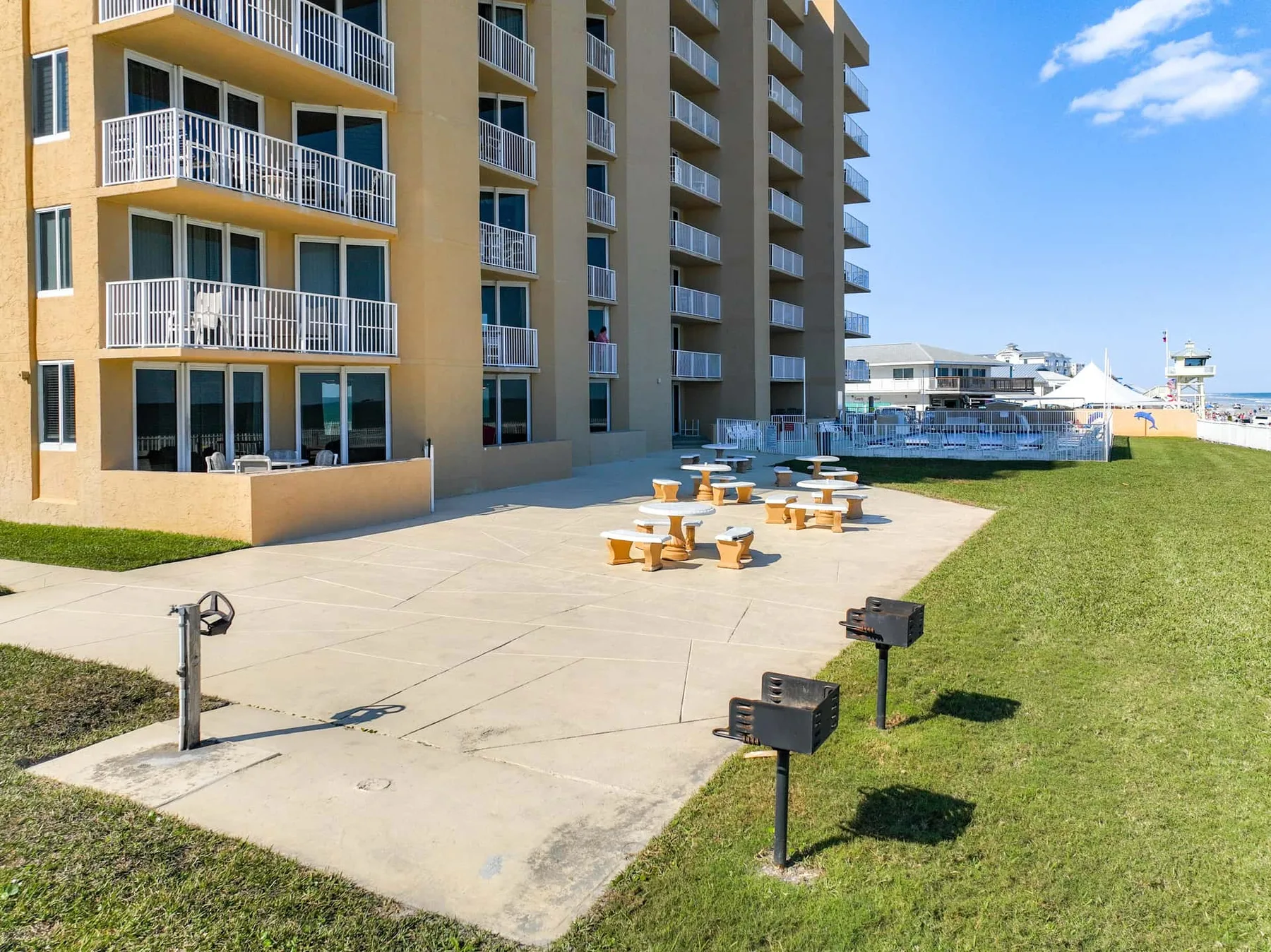 An outdoor patio beside a multi-story building has picnic tables and grassy lawn.